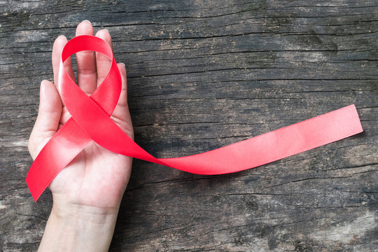 Red ribbon awareness (clipping path) on woman human hand aged wood background: World aids day campaign  to support people living with HIV STD heart disease