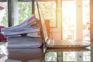 laptop and document stack on office desk with sun flare