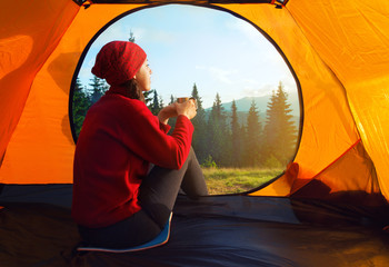 Girl sitting with cup inside orange tent looking at beautiful su