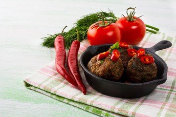 Grilled meatballs served with chili pepper slices in cast iron s