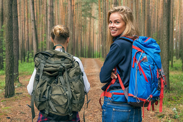 Blonde traveler with backpack smiling at camera near her girlfriend