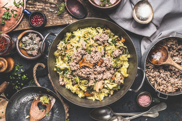 Casserole with rice , chopped cabbage and minced meat on rustic kitchen table with wooden spoons and bowls with flavoring and spices, top view.