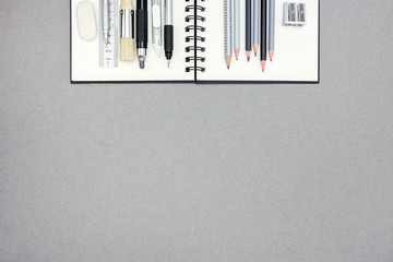 spiral notebook and various drawing tools on gray recycled paper
