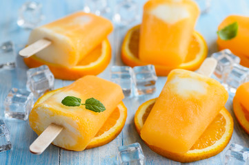 Homemade frozen ice cream popsicles made with oragnic fresh oranges on wooden background - obrazy, fototapety, plakaty