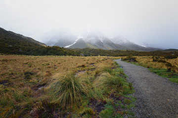 Gravel road leading to snow capped mountain which covered by thick fog.