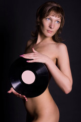 beautiful naked girl hiding her breasts behind an LP microgroove vinyl record on black background.