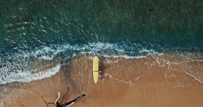 Aerial view of young woman paddling surfboard in blue ocean waves