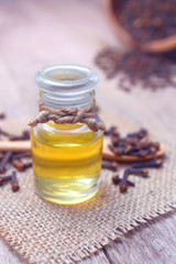 Essential aroma clove oil in a glass bottle with dried cloves on wooden spoon and background.