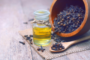 Essential aroma clove oil in a glass bottle with dried cloves on wooden spoon and background.
