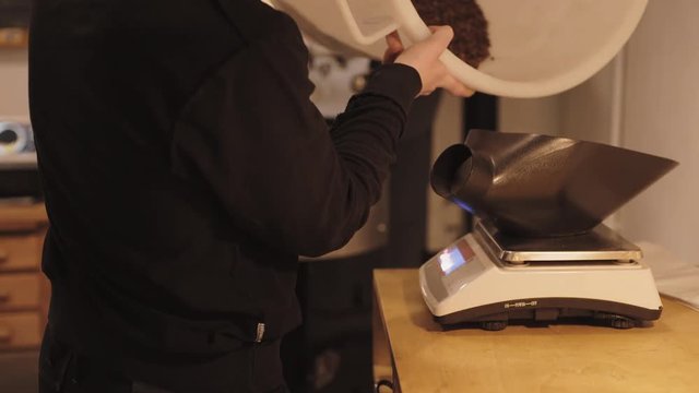 Man pours freshly roasted coffee beans from basket to weights before package and seal in small professional artisan coffee roastery lab