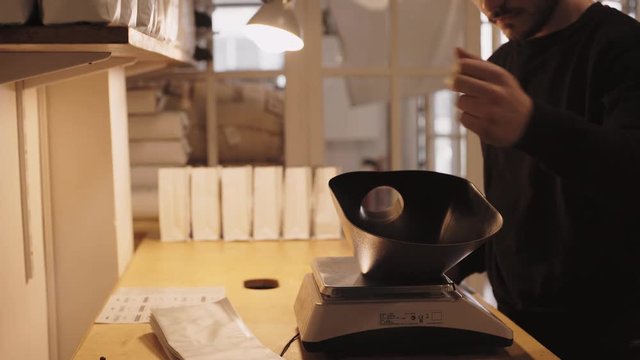 Man weights freshly baked coffee beans and pours it to small packages before seal and sale in small professional artisan roastery cafe lab