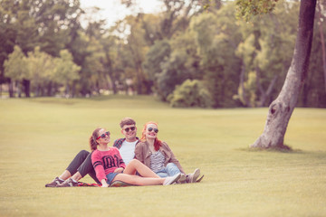 Friendship, leisure, summer and people concept. Group of smiling friends outdoors sitting on grass in park.