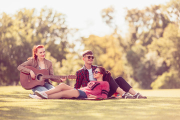 Group of friends with guitar having fun on picnic in park. Summer, holidays, vacation, music, happy people concept.