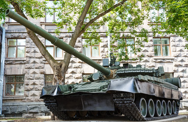military tank against the backdrop of a stone building summer sunny day