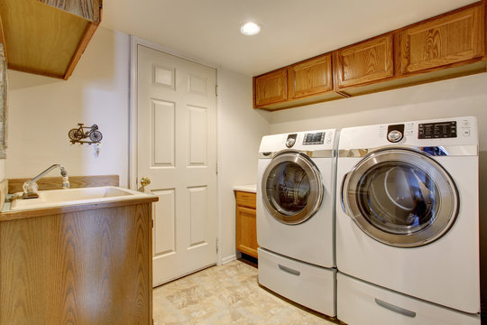 White laundry room interior with cabinets, sink and tile floor.