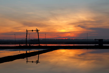 Fototapeta na wymiar SUNRISE AT SALT PAN The salt pans or salt evaporation pond reflected the the windmill in amber background because of sun rise in the early morning.