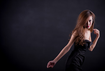 Fototapeta premium Beautiful sexy woman with perfect slim body and long curly hair in black dress posing over black background. Studio shot.