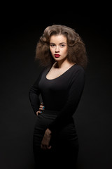 Fototapeta premium Portrait of beautiful lady in black dress posing with her arms folded or crossed. Pretty lady with red lips and modern hairstyle.