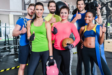 Group of women and men in gym posing at fitness training
