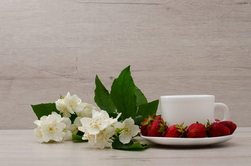 White mug, jasmine flowers and strawberries on a wood background