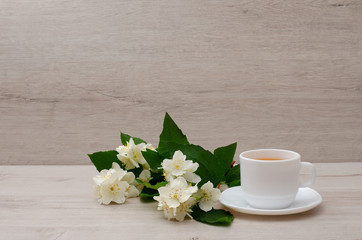 White mug with tea, a branch of jasmine on the wood background