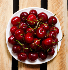 Red cherry in a plate on wooden boards, top view