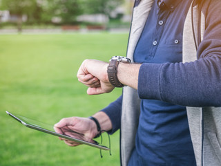 Young man looks at his watch and holding digital Tablet