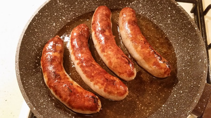 Appetizing ruddy juicy sausages fried in a large frying pan