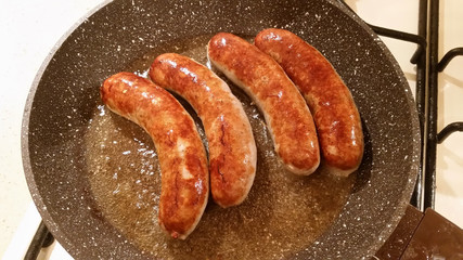 Appetizing ruddy juicy sausages fried in a large frying pan