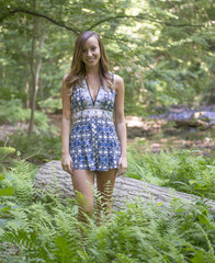 Beautiful young Caucasian woman wearing blue and white romper poses in woods