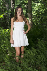 Beautiful young Caucasian woman wearing white sundress standing in the midst of ferns in forest