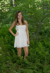 Naklejka na ściany i meble Beautiful young Caucasian woman wearing white sundress standing in the midst of ferns in forest