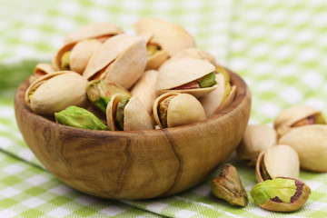 Pistachios in wooden bowl on green and white checkered cloth, closeup
