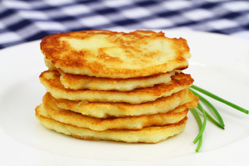 Potato fritters stacked up on white plate and chives garnish
