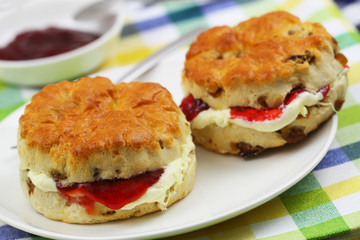 Freshly baked English scones with clotted cream and strawberry jam on checkered cloth
