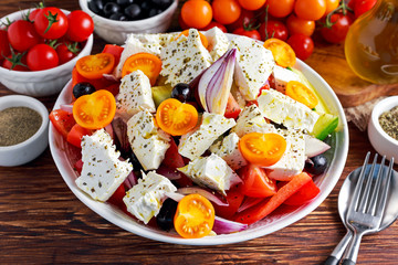 Greek salad with fresh sweet pepper, red onion, orange cherry tomatoes, cucumber, black olives and feta chees drizzled extra virgin olive oil on wooden table