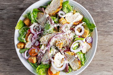 Ceasar salad with grilled chicken fillets, red onion rings, lettuce, orange cherry tomatoes, croutons, grated parmesan cheese, seasoned  anchovy 