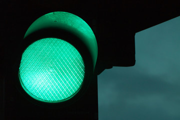Green traffic light by night and dark sky at the background