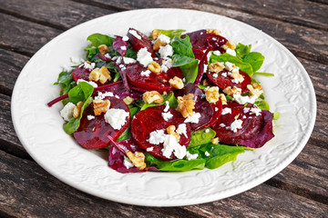 Healthy Beet Salad with fresh sweet baby spinach, kale lettuce, nuts, feta cheese on wooden table.