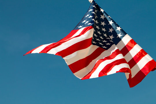 United States flag blows in the wind against a blue sky attached to the wall from the side.