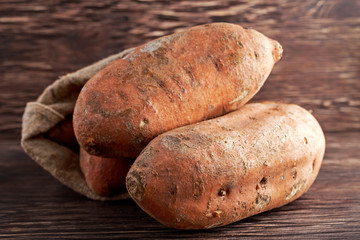Freshly harvested organic sweet potatoes in a burlap bag on wooden table.