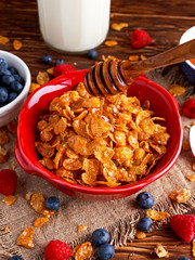 Corn Flakes with berries raspberries, blueberries, milk, and sweet pouring honey.
