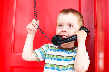 child holding a telephone receiver and smiling. cute boy talking on the phone in a red telephone box.
the concept to share with the family joy and impressions