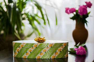 Green gift box on the table on the background of flowers 