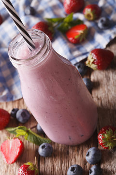 milk smoothie with strawberries and blueberries in a glass bottle close-up. vertical
