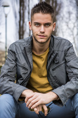 Obraz premium Portrait of handsome young man looking to a side while sitting in city park