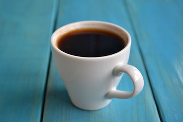 A white porcelain cup of black coffee is on the blue wooden table. Rustic still life.