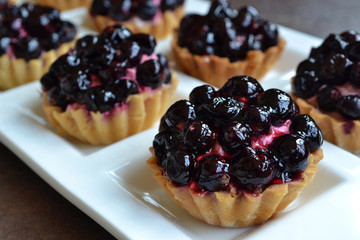 Close up of small fruit tart with cream filling. Mini cakes with black currant are in the white porcelain plate. Soft focus.