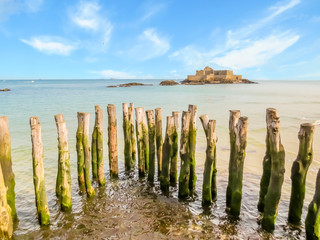 Wooden breakwaters in high flow and Fort National - obrazy, fototapety, plakaty