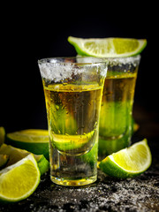 Mexican Gold Tequila with lime and salt on black table. Two Tequila shots. Alcohol drink.